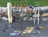 Photo of long bar clamps with orange handles, C-clamps, push sticks, doweling jig, a small drill gauge tool, and two sets of Rockler bench cookies in packaging