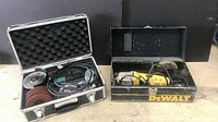 Two angle grinders side by side, one in an aluminum carrying case with accessories and the other in a black metal DeWalt box.