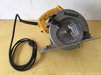 Full side view of the DeWalt DW358 circular saw showing yellow handle with attached black cord and metal blade guard resting on a yellow surface.