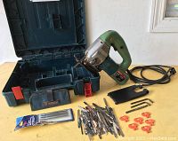 Bosch 1581VS jigsaw with cord, multiple blades, Allen wrenches, blade holder, and hard plastic carrying case all laid on a table.