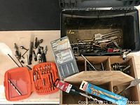 Photo showing the overall lot including the rustic wooden compartment box, heavy-duty black plastic case, and various bits scattered around.