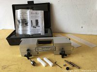 Full view of the Hinge Mate HM1100W tool in hard case open with manual documents, two plastic spacers, metal pins and the aluminum hinge template tool with knobs visible.