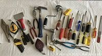 Photo showing assortment of small hand tools including hammer, pliers, screwdrivers, vintage drill, and measuring tools.