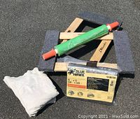 Photo showing two padded furniture trolleys stacked with shrink wrap roll, drop cloth, and Blue Hawk tarp in packaging on an asphalt surface.