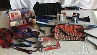 Wide view of the car tools and safety supplies laid out on a white surface showing wrecking bars, wrench set, straps, gloves, goggles, and first aid kit.
