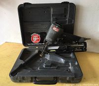 Full view of Senco angled finish nailer placed inside a hard plastic carrying case on yellow surface.