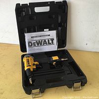 DeWalt pneumatic nailer in black hard case with manual insert inside case lid, case open and placed on flat surface