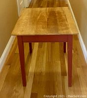 Square side table with natural wood top, red painted legs and frame, shows wear on legs.