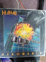 Photo of the cover of the Def Leppard Pyromania 1983 vinyl album showing artwork of a building explosion and crosshairs, in plastic sleeve.