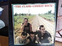 Photo showing the album cover of 'Combat Rock' by The Clash with band members near railroad tracks.