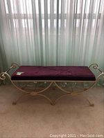 Full front view of metal bench with purple velvet seat showing the curved scrollwork metal base and cushion.
