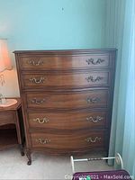 Front view of the solid wood highboy dresser showing five drawers with curved fronts and decorative brass handles.