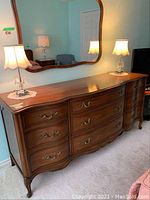 Front and angled view of solid wood dresser showing drawer layout and ornate metal handles.