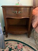 Front view of bedside table showing single drawer with ornate brass-tone handle and open shelf