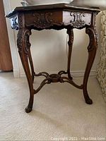 Front and side view of carved wood occasional table showing ornate apron and legs with floral inlay.