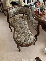 Front and angled view of antique curved settee with floral upholstery and wooden frame showing upholstery details and leg style.