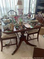 Overall view of dining table top with various items placed on top, showing wood finish and chairs partially visible.