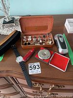 Full lot arranged on wooden surface showing cufflinks in case, wristwatch, Swiss Army knife, brush, pitch pipe, shaving brush, and shaver.