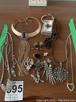 Wide shot of all jewelry arranged on wooden surface showing necklace, earrings, brooches, bracelet mostly silver-tone and some gold-tone pieces with various embellishments.