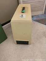 Closed beige hard carrying case for Singer sewing machine with handle and Singer branding on front.