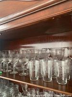 Shelf displaying multiple etched stemware glasses and juice glasses in clear glass with vintage etched patterns.