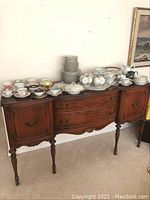 Front view of antique wooden sideboard buffet cabinet with plates and china on top.