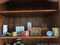 Wooden shelf displaying various vintage children's boxed games and card games including Brain Quest, the Famous Five, Nesting Cubes, Twin Kins and others.
