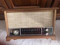 Front and angled view of vintage Zenith AM FM radio showing wood grain finish, fabric speaker cover, horizontal frequency display and tuning knobs.