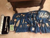 Full view of the silverplated flatware and serving pieces arranged on a blue fabric roll and cloth, showing variety and quantity.