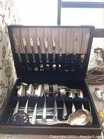 Full view of the blue felt-lined case opened, showing rows of knives stored on the lid and forks, spoons arranged in the bottom compartments.