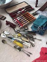 Photo of the full collection showing knife sets, various flatware and utensils, and silverware bags on a carpeted floor.