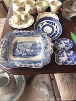 Top view of antique blue and white platter, trinket dishes, plate, and assorted mugs on wooden table