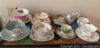 Overview of eight assorted bone china tea cups with saucers, creamer, and sugar bowl