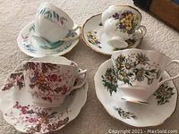 Four bone china tea cups and matching saucers with different floral patterns and gold trim