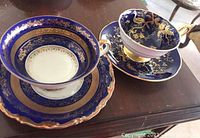 Two tea cups and saucers on wood surface, showcasing cobalt blue and gold design from Coalport and Kunst Kronach Bavaria.