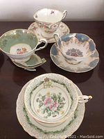 Four sets of tea cups and saucers on a table including the green floral ER crown set, blue and gold set, and two floral sets.