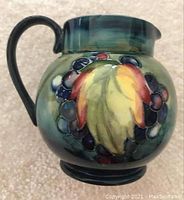 Side view of the Moorcroft jug showing the colorful leaf and berry design and dark green handle.