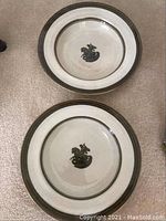 Two cream-colored ceramic bowls with black St. George and dragon motif, top view