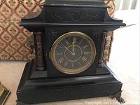 Front view of antique black wooden mantel clock with brass bezel and Roman numeral dial.