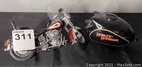 Franklin Mint 1:10 scale Harley Davidson Heritage Softail Classic motorcycle model with detached Harley Davidson ceramic fuel tank piggy bank on a table. Headlight on the motorcycle is detached.