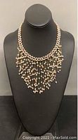 Full view of the necklace on black mannequin showing base strand and hanging pearl strands.