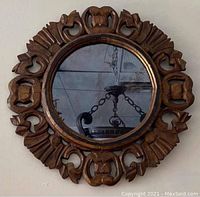 Front view of the round mirror showing the detailed hand carved wooden frame and mirror glass reflecting a chandelier.