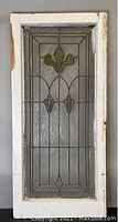 Front view of antique leaded stained glass window showing colored floral motifs and textured glass with geometric lead delineation.