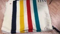 Folded blanket top view showing four coloured stripes on cream ground