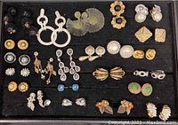 Overview of multiple pairs of costume earrings arranged in rows on black display including various colors, shapes, and styles.