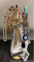 Assorted costume jewelry including bangles, faux pearl and bead necklaces hanging on the jewelry stand covered with silver fabric.
