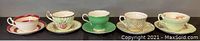 Front view of five teacups and saucers of varied decorative styles displayed in a row on a black surface.