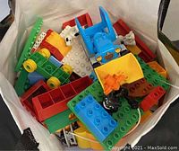 Photo of assorted medium-sized LEGO bricks including wheels, flat plates, and vehicle parts in primary colors inside a white container.