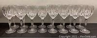 Front view of 16 clear ribbed crystal wine goblets, two rows of 8 each, showing ribbed design and round bases on black background.