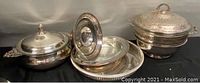 Multiple silver plated serving items displayed together, showing lidded bowls, tray and pedestal plate.